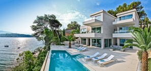A modern two-story house with a swimming pool, lounge chairs, and a view of the sea. - Beachfront Villa Seven Sins with Pool (Selca)