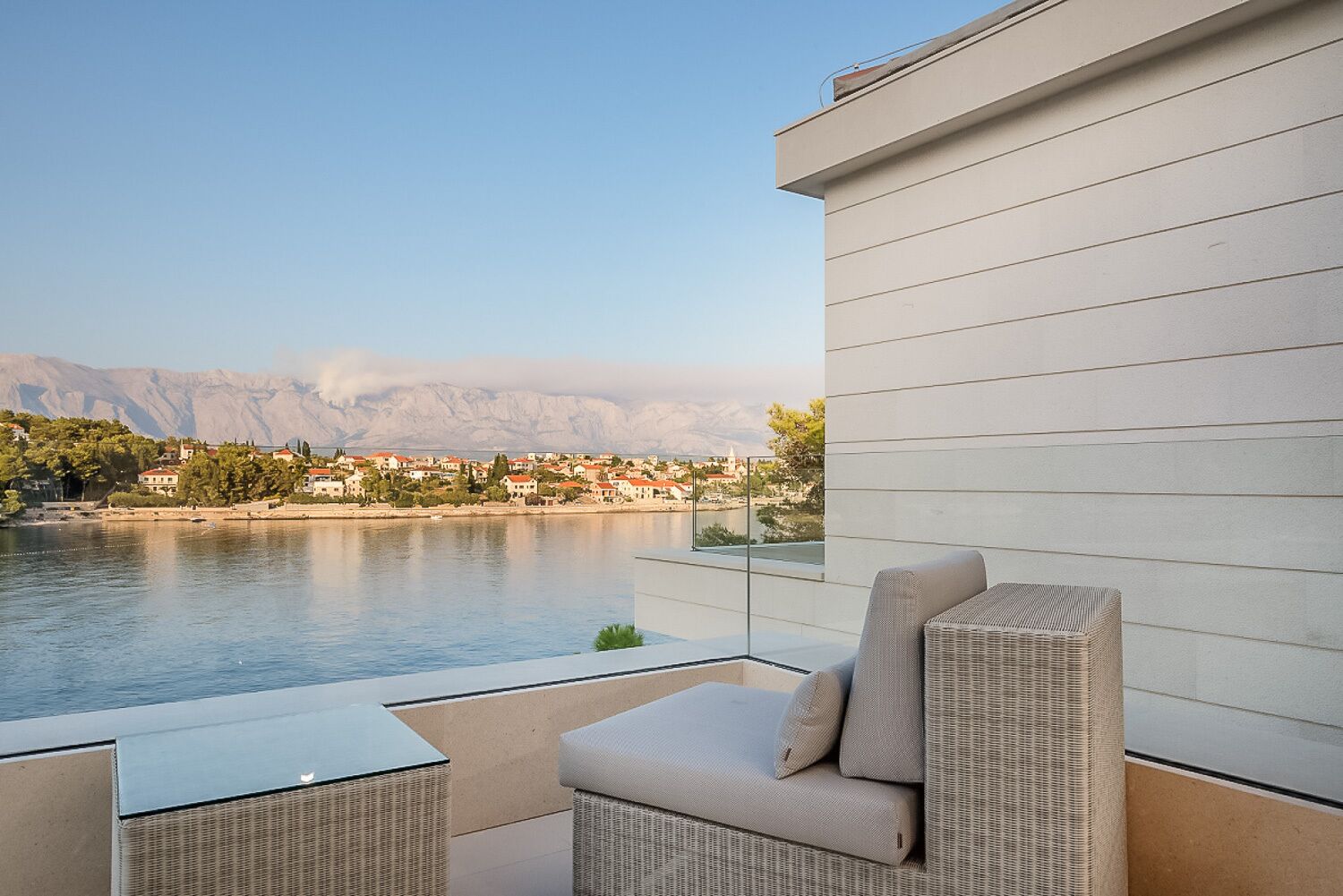 A balcony with wicker furniture, a view of a lake, and buildings in the background.
