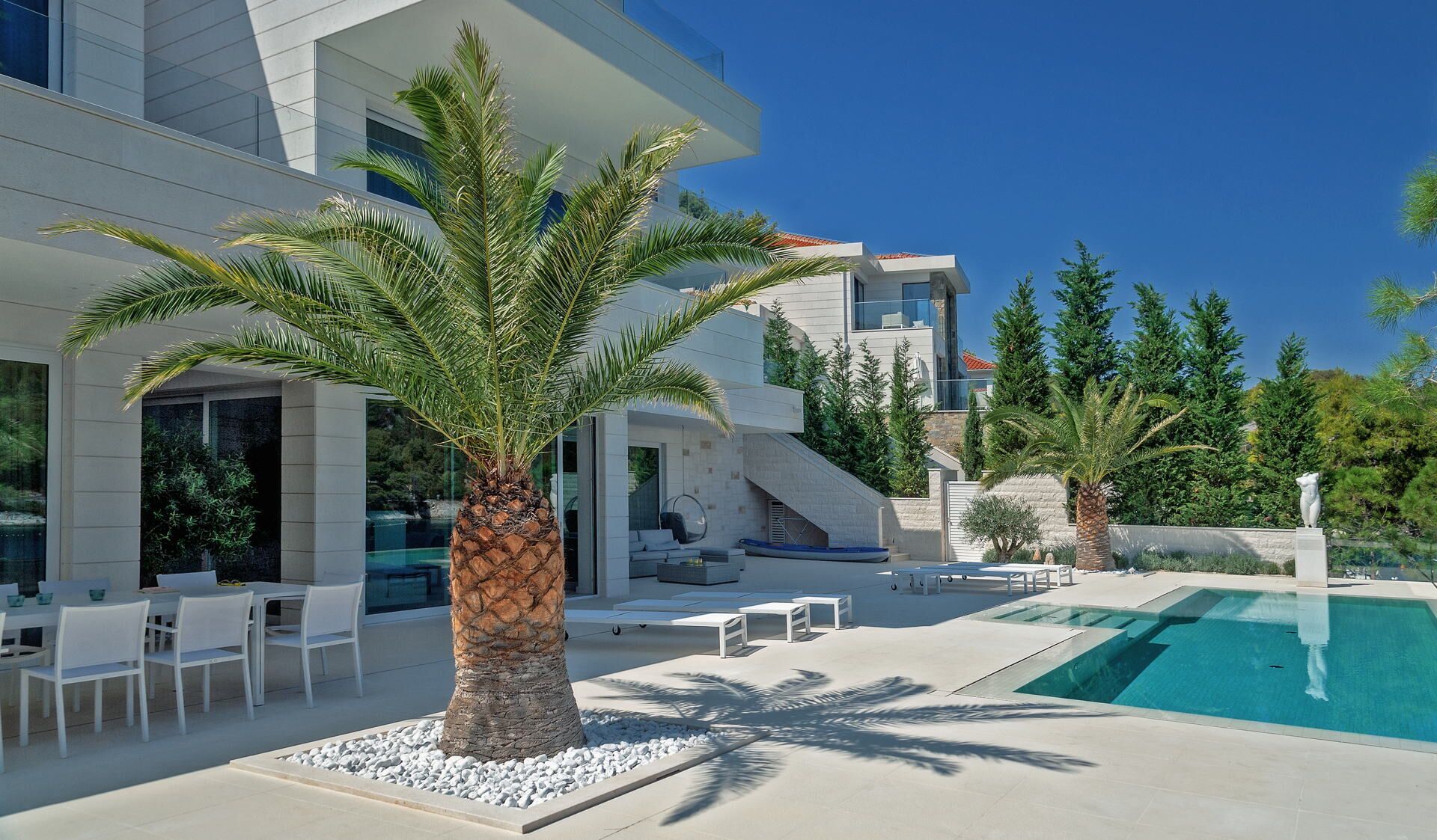 A modern house with a swimming pool, outdoor seating, and palm trees.