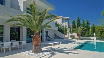 A modern house with a swimming pool, outdoor seating, and palm trees.