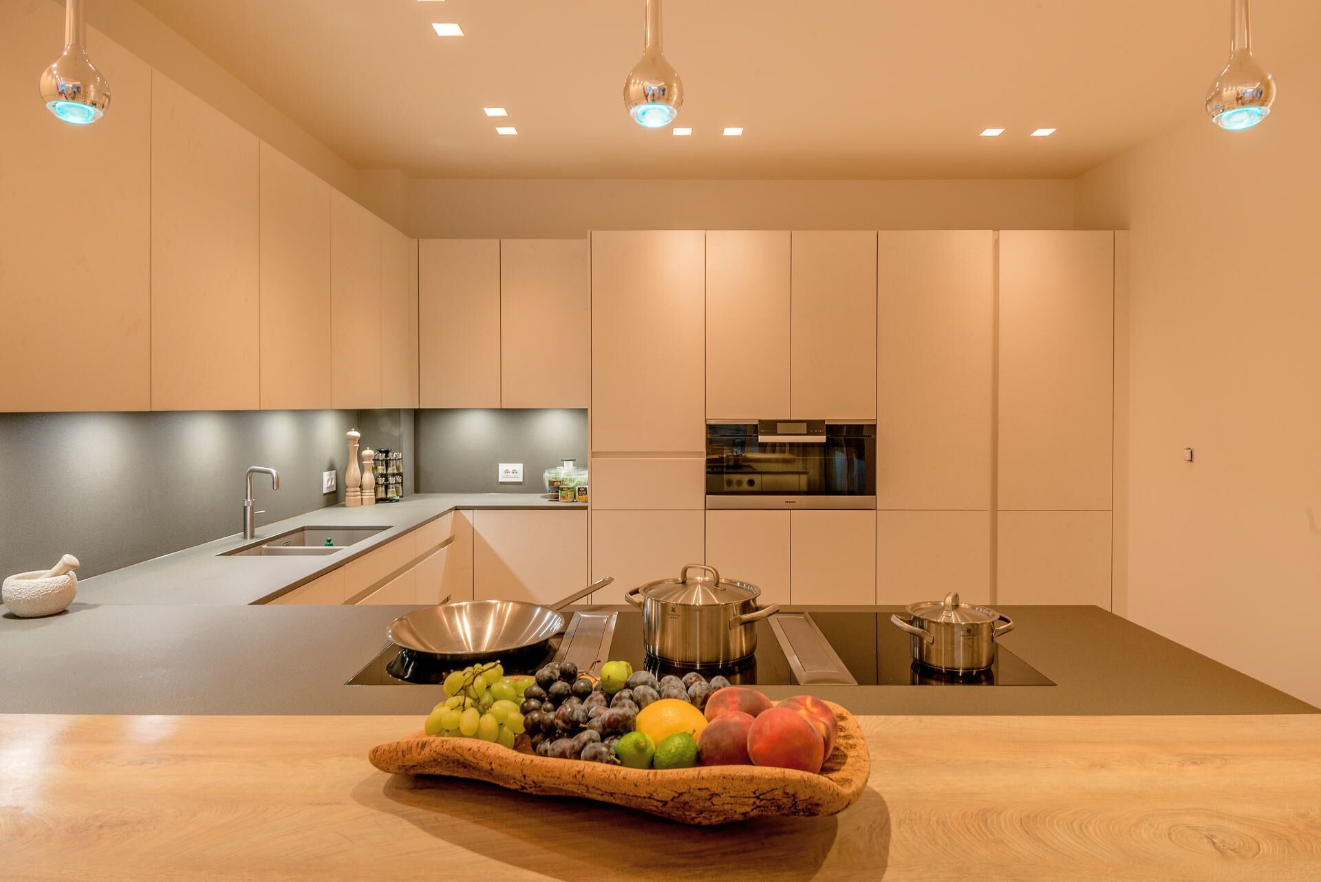 Una cucina moderna con isola centrale, elettrodomestici in acciaio inossidabile e una selezione di frutta e verdura sull'isola.