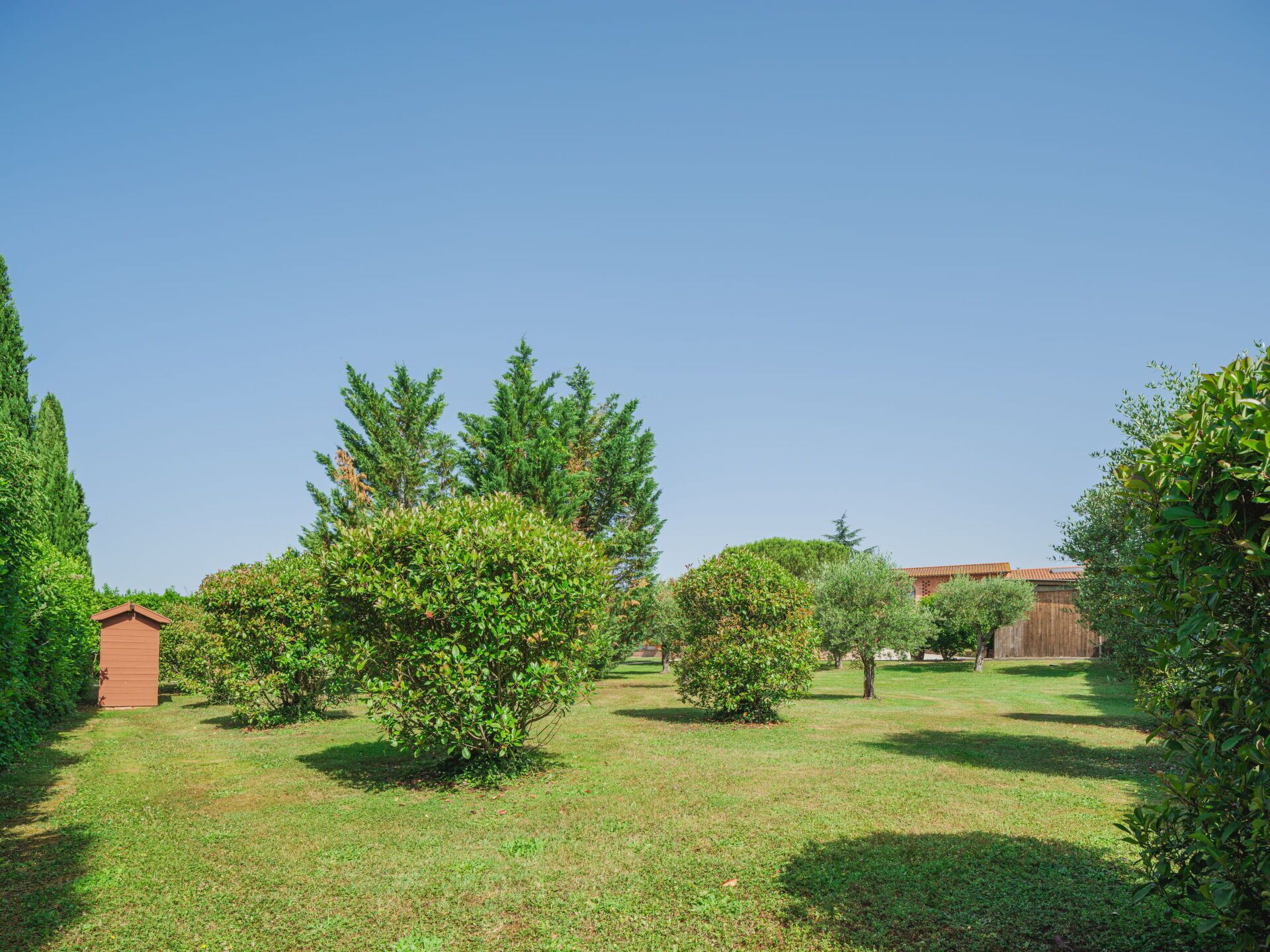 Un giardino curato con diversi alberi e arbusti, un recinto in legno e un piccolo edificio.