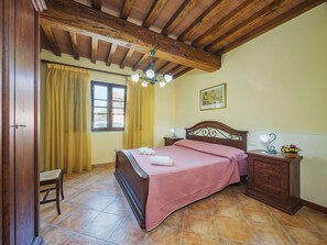 Traditional hotel room with a wooden bed, nightstand, and table, featuring a framed picture and a vase of flowers.