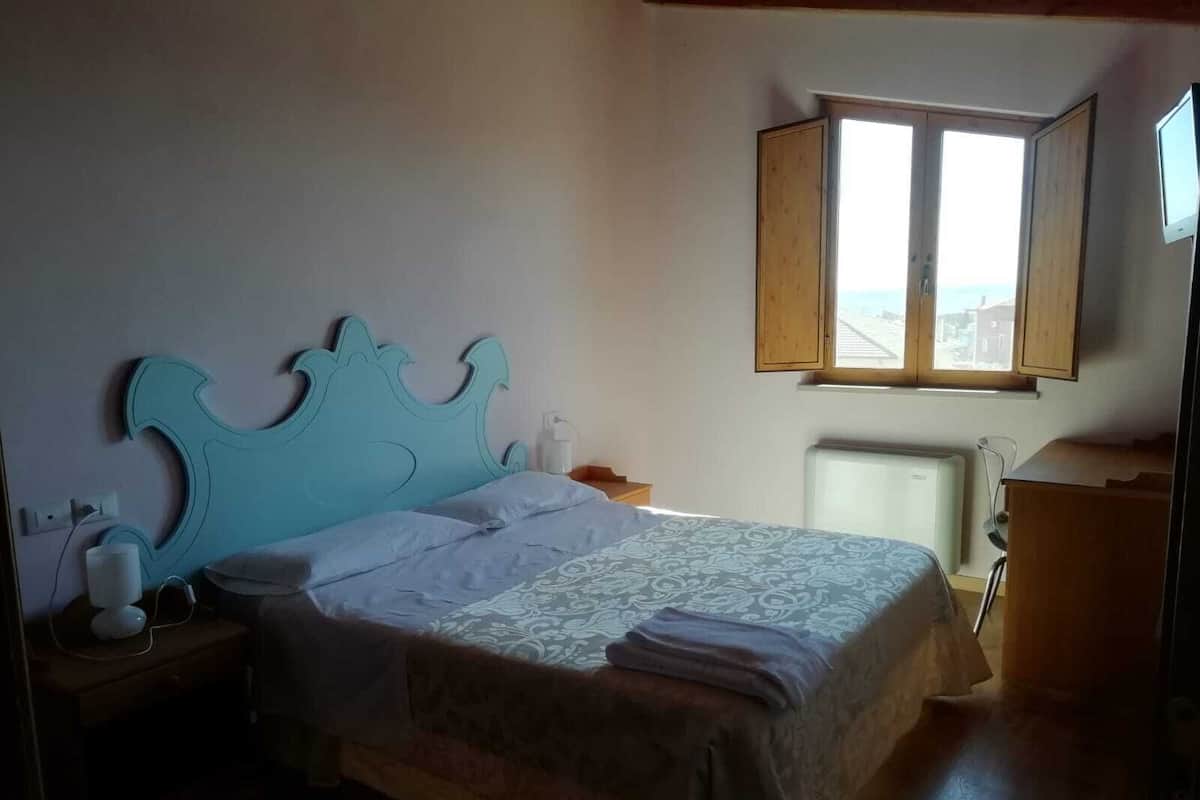 A bedroom with a large bed, a nightstand, a dresser, a window, and a radiator.