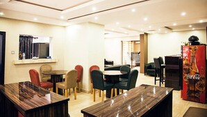 A modern dining area with multiple tables and chairs, a refrigerator with a Coca-Cola logo, and a window with curtains. - Lantano Cottage (Lagos)