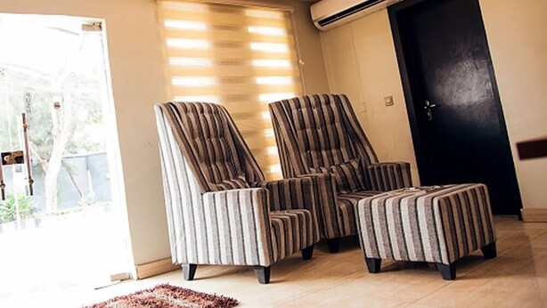 A living room with striped armchairs and ottoman, a black door, and an air conditioning unit on the wall. - Lantano Cottage (Lagos)