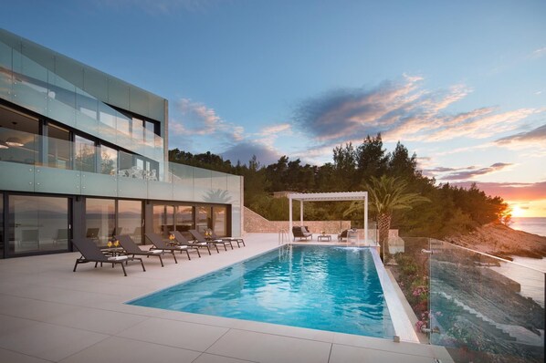 Un área de piscina moderna con piscina cubierta con vidrio, sillas de descanso y una pérgola.