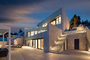 Una casa moderna con fachada de vidrio, revestimiento de piedra y una escalera que conduce al nivel superior.
