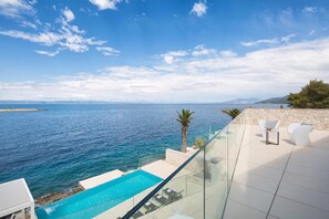 Un área de piscina moderna al aire libre con vistas despejadas al mar y montañas al fondo.