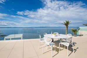 Una terraza con una mesa redonda y sillas blancas, con vista a una masa de agua y una isla distante.