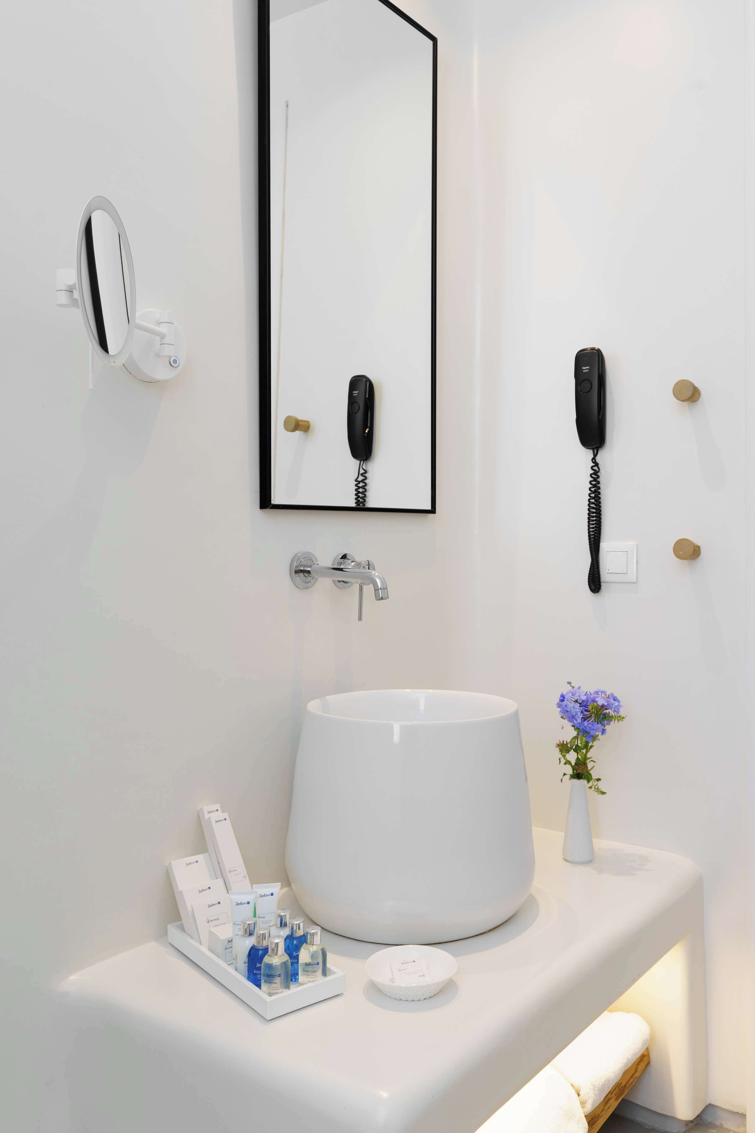 Un baño moderno con un lavamanos blanco grande, un espejo, un teléfono y artículos de tocador en la encimera.