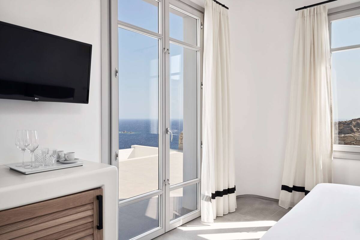A hotel room with a large sliding glass door leading to a balcony with a view of the sea.