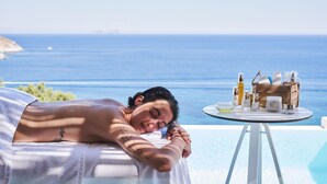 A person relaxing by a pool with a view of the sea, a table with skincare products, and a towel. - Radisson Blu Euphoria Resort, Mykonos (Mykonos)
