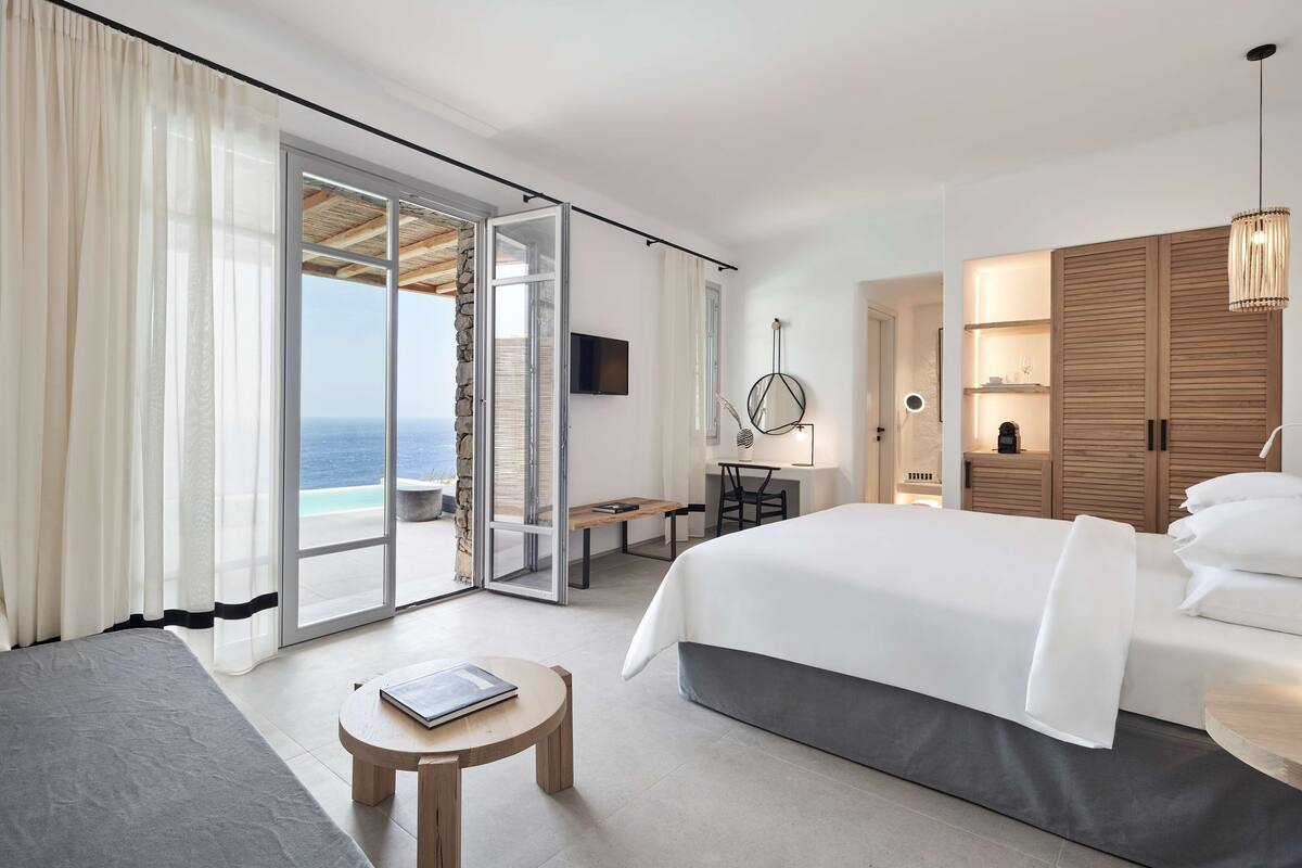 A modern hotel room with a large bed, a desk, and a view of the ocean.