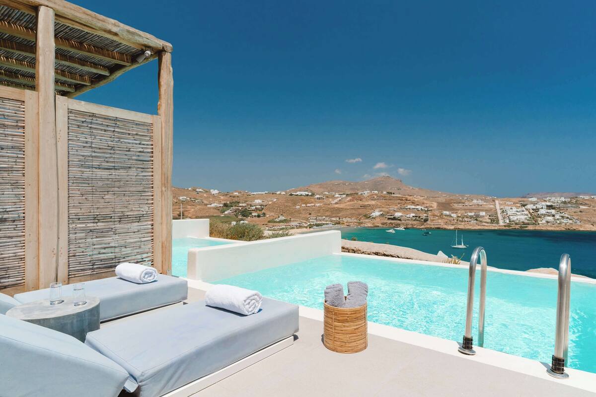 An infinity pool with a view of the sea and a mountainous landscape.
