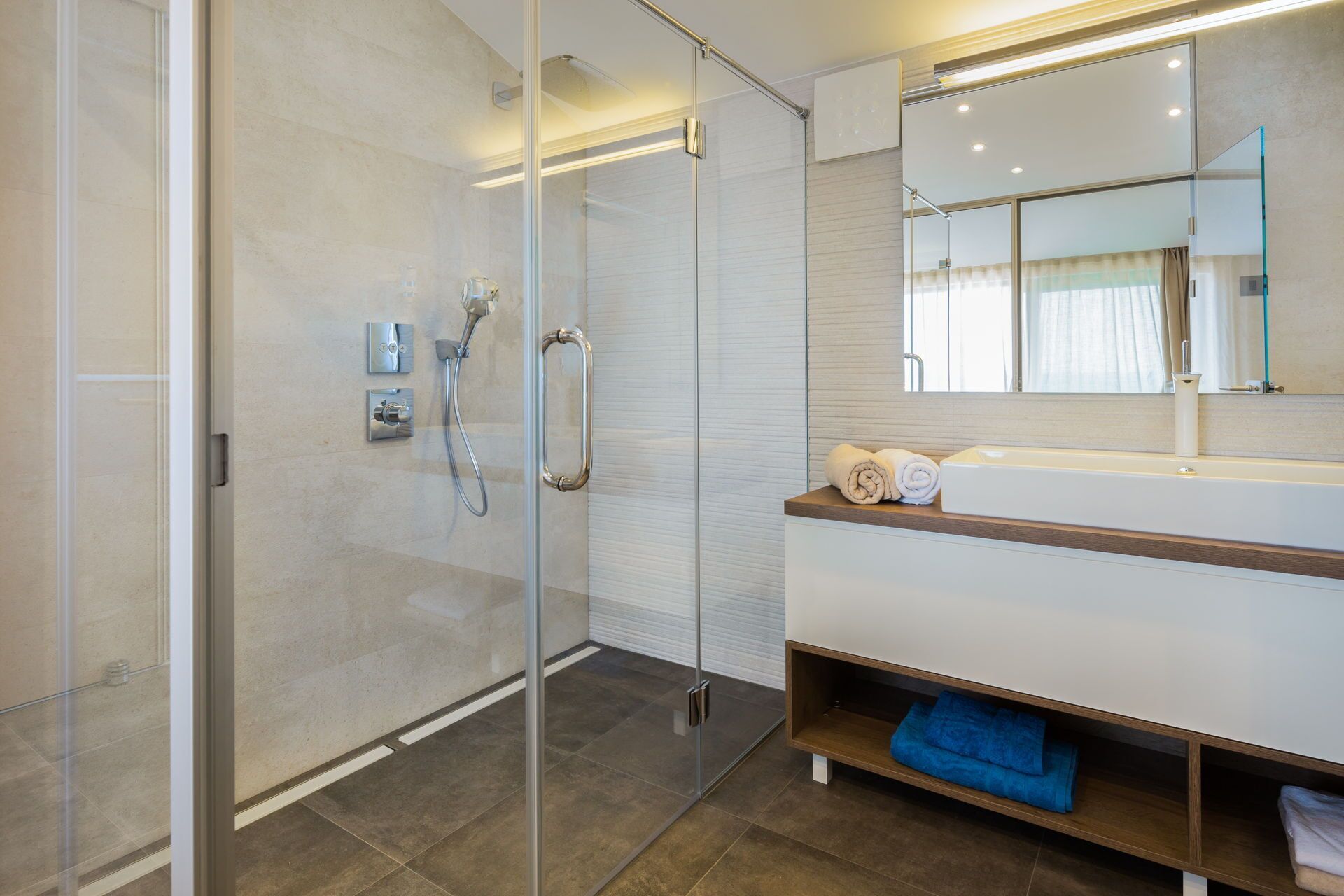 A modern bathroom with a glass shower enclosure, a white vanity with a mirror, and a blue towel on the shelf.