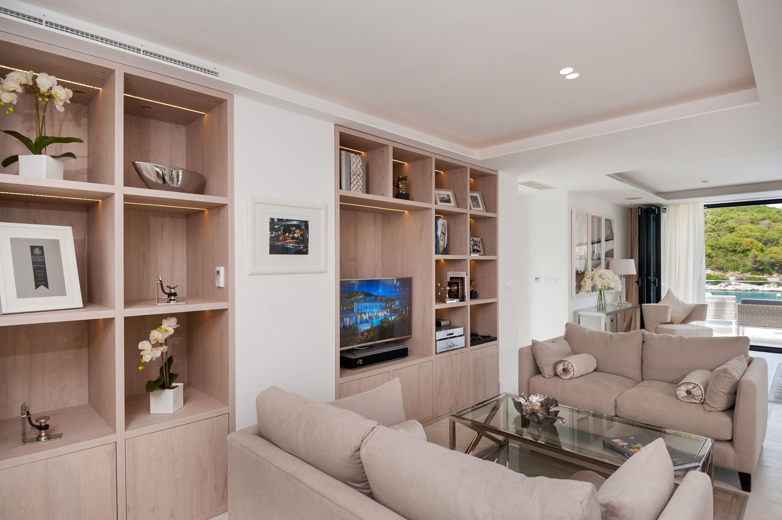 A modern living room with built-in wooden shelving, a flat-screen TV, and a glass coffee table.