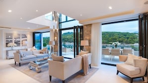 A spacious living room with a large window offering a view of a lake and hills. There are multiple seating areas, including a sofa and armchairs, and a coffee table. - Luxury Villa Silent with Infinity Pool (Selca)