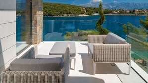 A balcony with wicker furniture, a glass barrier, and a view of a lake and mountains. - Luxury Villa Silent with Infinity Pool (Selca)
