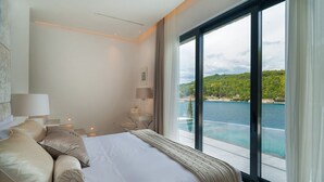 A modern bedroom with a large bed, bedside tables, and a view of a body of water. - Luxury Villa Silent with Infinity Pool (Selca)