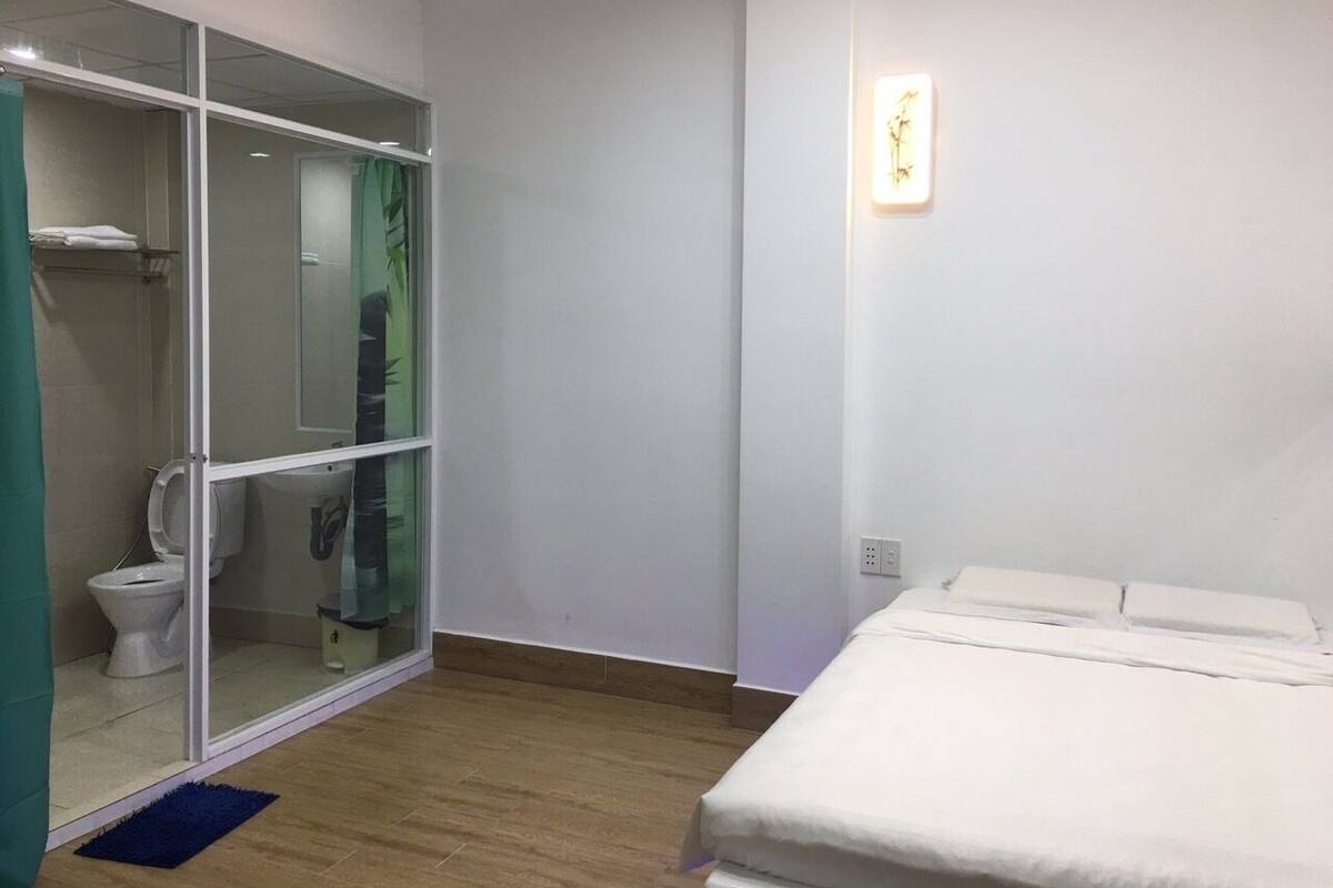 A room with a bed, a glass-enclosed shower area, and a white wall with a light fixture.
