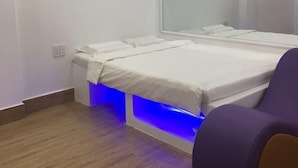 A modern bedroom with a bed, a bedside table, a chair, and an air conditioning unit. - Mai Tuan Pham Hung Hotel (Hoa Thanh)