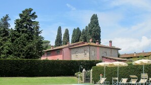 A pool area with lounge chairs and umbrellas, surrounded by a well-maintained lawn and a large building with a pink facade and stone accents. - Nice apartment in villa for 2 people with pool, A/C, WIFI, TV and terrace (Lucca)