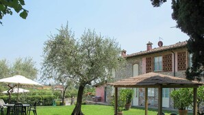 An outdoor seating area with tables and chairs, surrounded by greenery and a stone building. - Nice apartment in villa for 2 people with pool, A/C, WIFI, TV and terrace (Lucca)