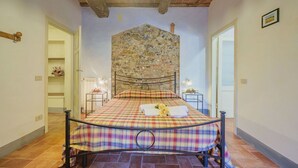 A bedroom with a stone wall, a bed with a plaid bedspread, and a wooden ceiling. - Nice apartment in villa for 2 people with pool, A/C, WIFI, TV and terrace (Lucca)