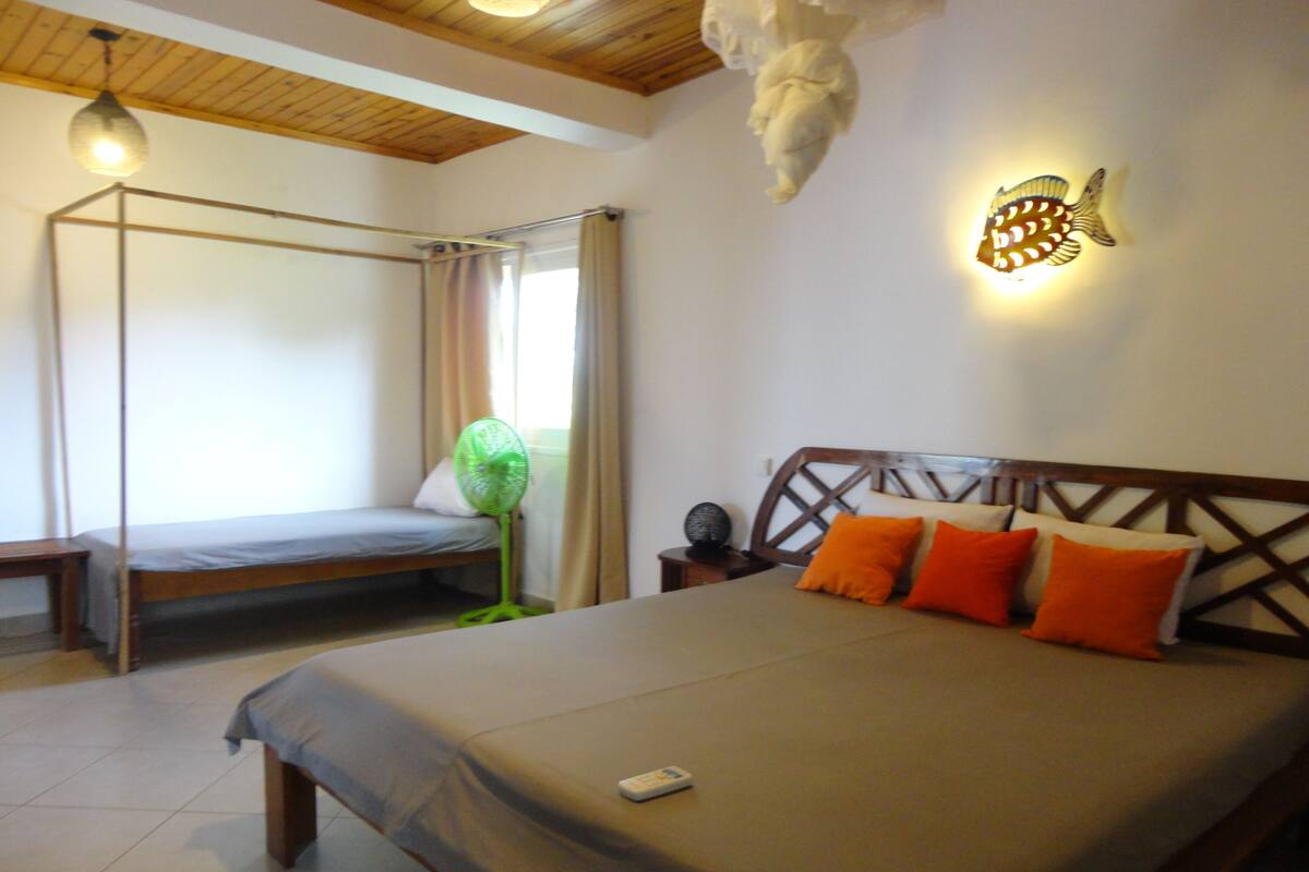 A bedroom with a bed, a daybed, a standing fan, and a wall-mounted light fixture.