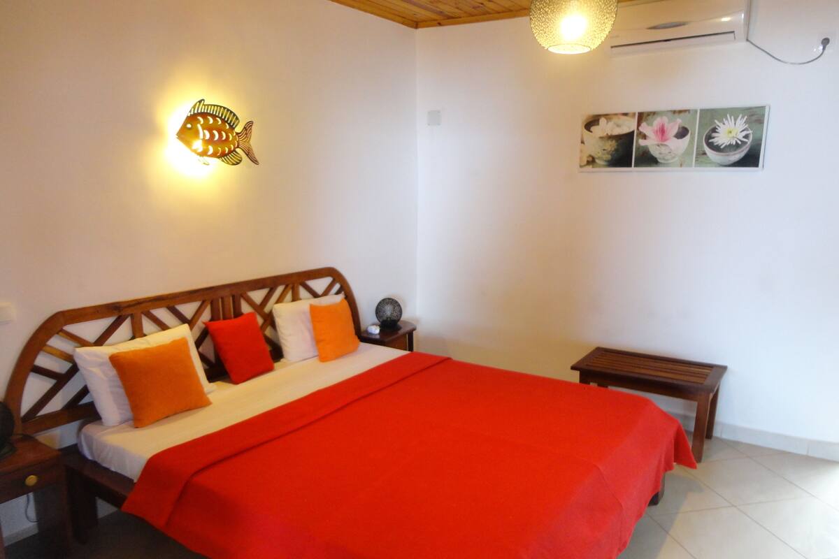A bedroom with a wooden bed, red bedding, a wall-mounted fish light, and a small bedside table.