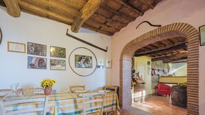 A rustic dining area with a checkered tablecloth, wooden chairs, and a brick archway leading to another room.