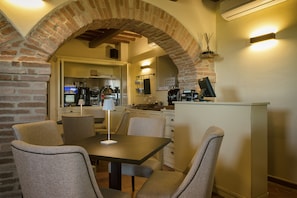 A dining area with a brick archway, a table with chairs, and a kitchen in the background.