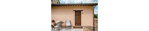 A small outdoor patio with a table and chairs, a door, and a view of the countryside.