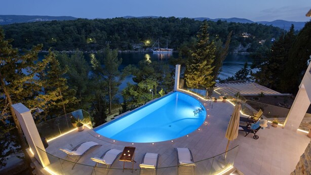 A swimming pool with a glass balustrade, lounge chairs, and a view of a lake and forested hills. - Luxury Villa Hvar Enigma with Pool (Jelsa)