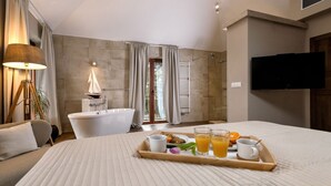 A bedroom with a bed, a bedside table with a tray of breakfast, a bathtub, a shower, and a TV mounted on the wall. - Luxury Villa Hvar Enigma with Pool (Jelsa)