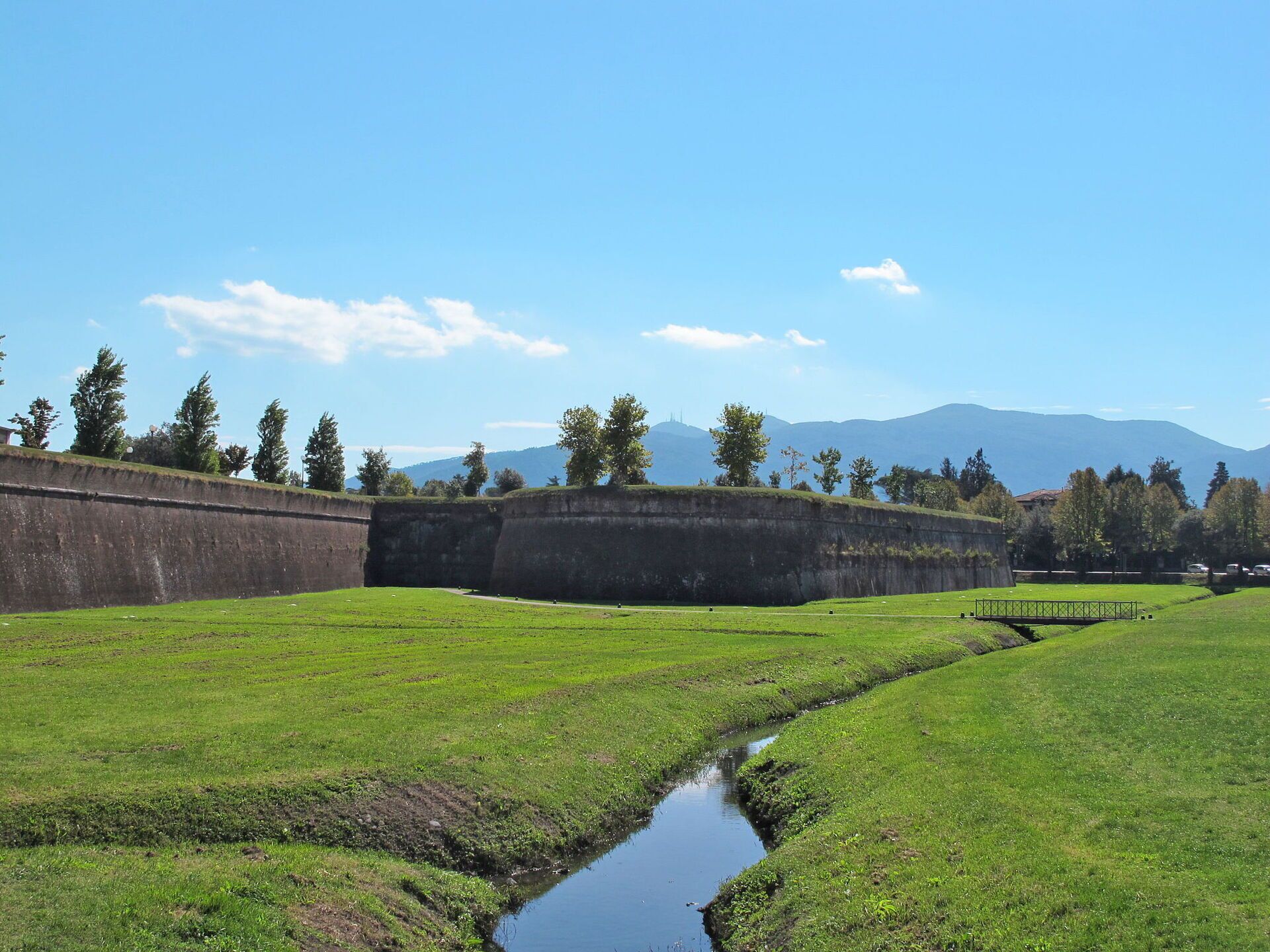 A grassy field with a small stream and a stone wall.