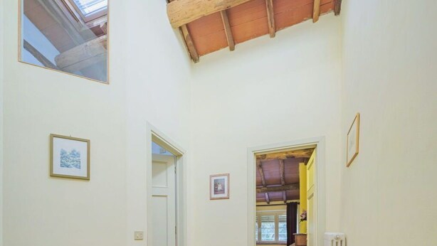 A corridor with a tiled floor, wooden ceiling beams, and framed pictures on the walls.