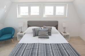 Une chambre à coucher avec un lit, deux tables de chevet, une chaise et deux fenêtres.