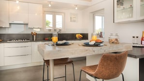 Eine moderne Küche mit Kochinsel, Barhocker und einer Frühstücksecke mit Orangensaft und Obst.