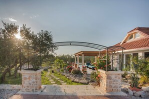 Un sentier de jardin mène à un espace extérieur abrité, aménagé avec des piliers en pierre et des plantes en pot.
