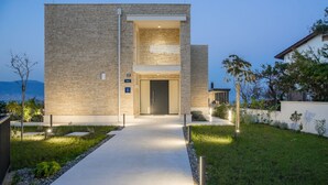 A modern building with a stone facade, a central entrance, and a well-maintained lawn. - Beachfront Villa Grey Martini with Pool (Split)