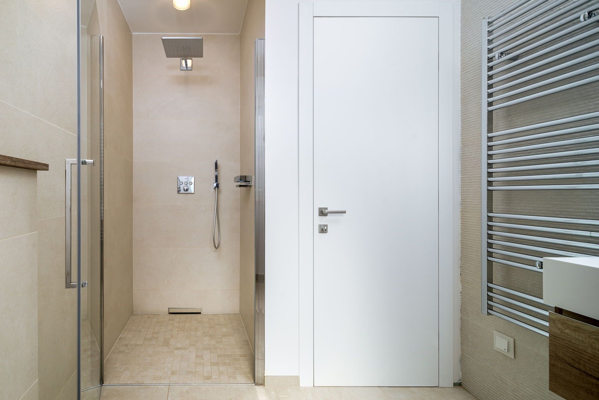 Een moderne badkamer met een douchecabine van glas, een witte deur en een handdoekhouder met horizontale stangen.