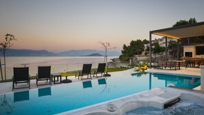 A poolside area with lounge chairs and a hot tub, overlooking a body of water with mountains in the distance. - Beachfront Villa Grey Martini with Pool (Split)