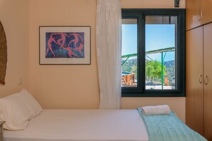 Ein Schlafzimmer mit einem Bett, einem Fenster mit Blick auf eine grüne Außenanlage und einem gerahmten Kunstwerk an der Wand.