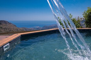 Ein Infinity-Pool mit Holzterrasse und Blick auf Ozean und Berge.