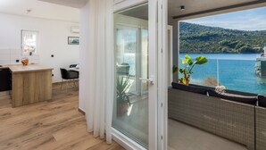 A modern living room with a wooden floor, a glass door leading to a balcony with a view of a lake and hills. - Beachfront Villa Seashell with Pool (Marina)