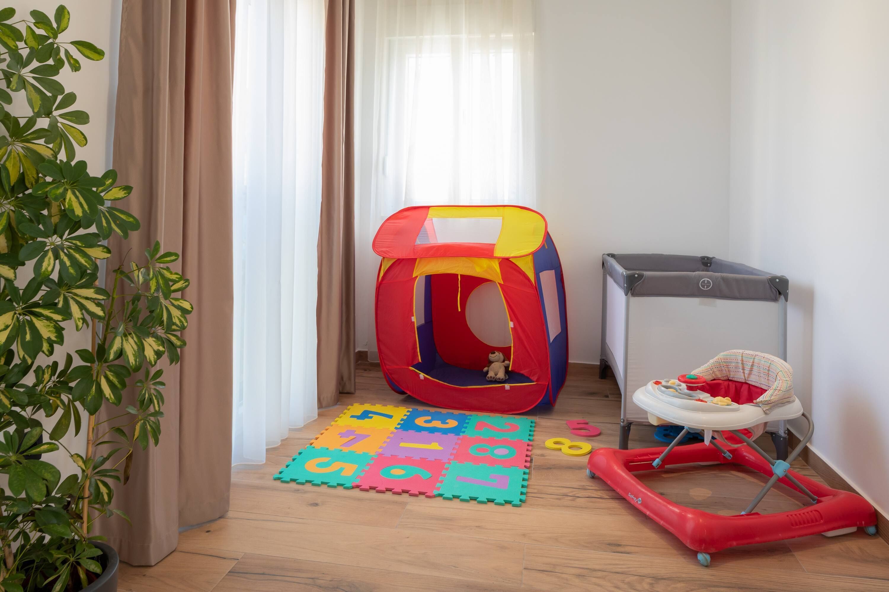 Zona de juegos con una carpa, un andador y una colchoneta con números.