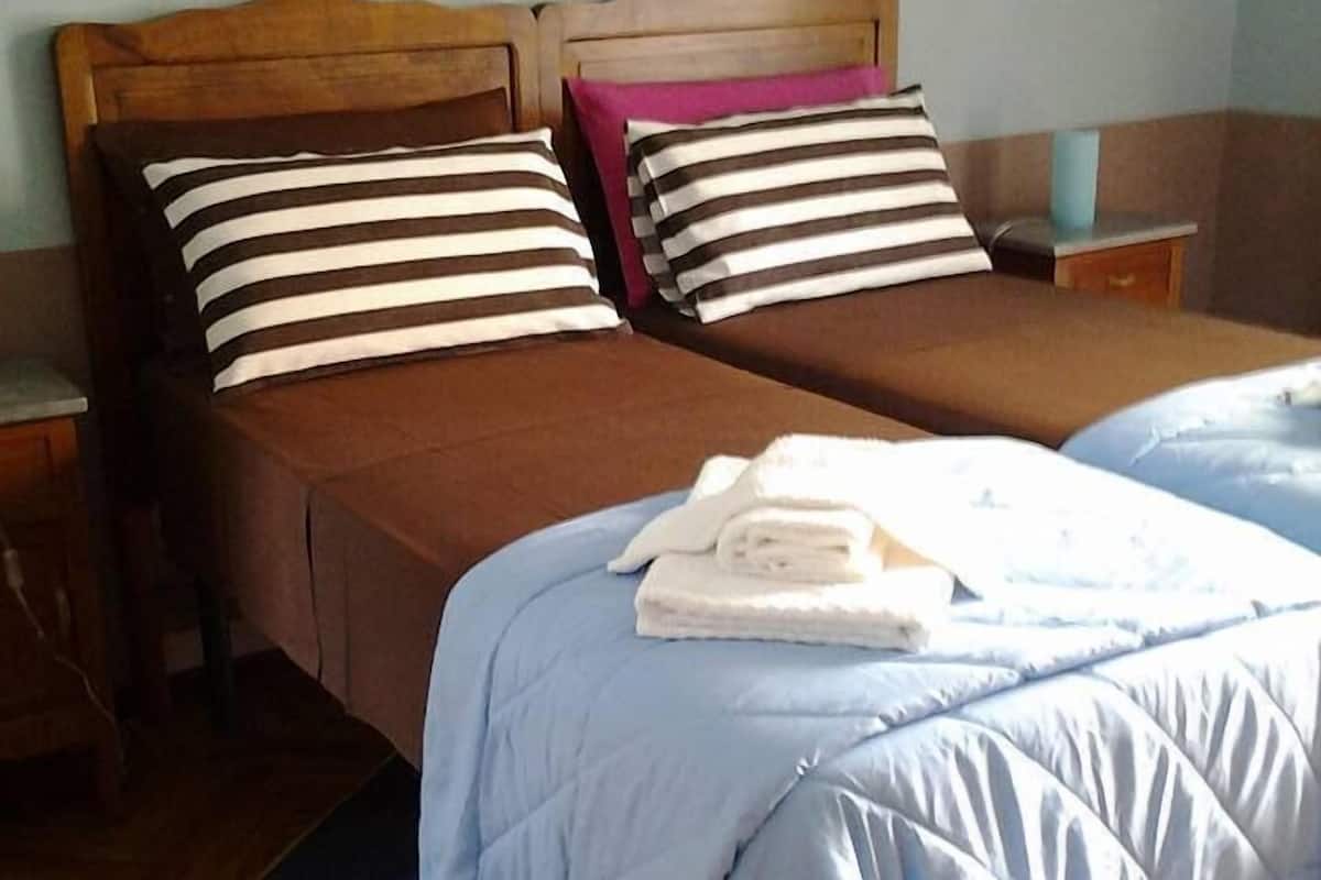 A double bed with striped pillows, a blue quilted duvet, and a folded towel on the bed.