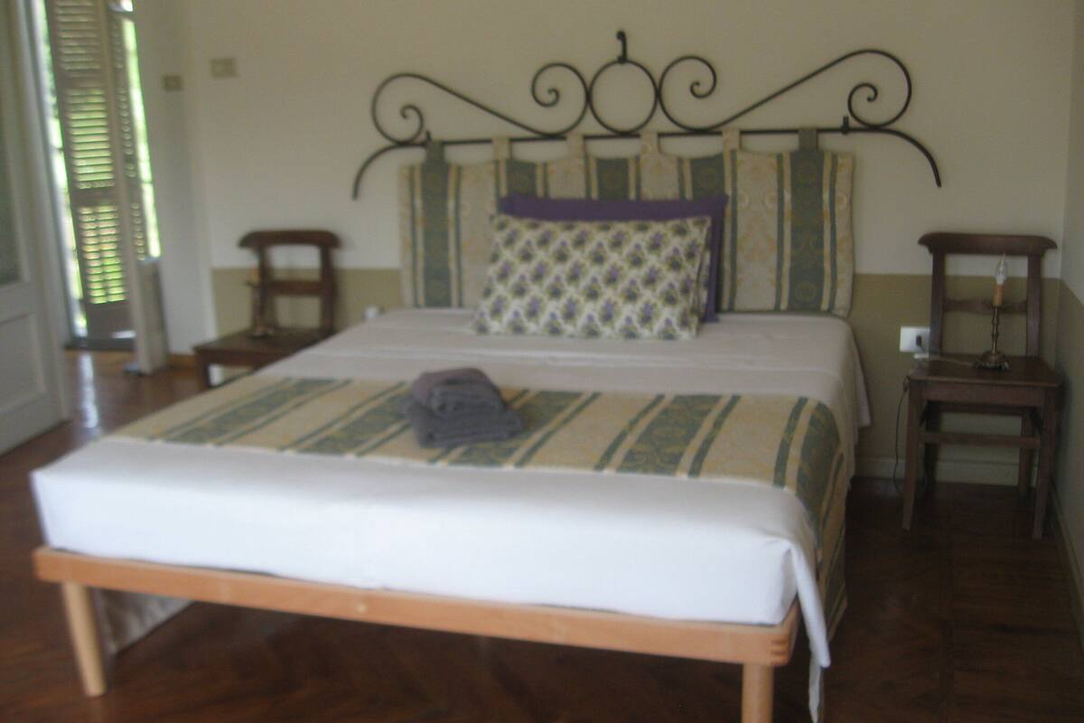 A neatly made bed with a wooden frame and a white mattress, a patterned pillow, and a bedside table with a lamp.